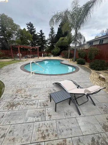 View of swimming pool featuring patio surround, a fenced backyard, and a pergola