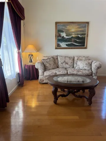 Hardwood-finish flooring throughout, featuring a large window with drapes, and neutral wall tones