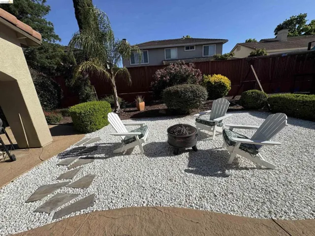 Landscaped backyard featuring white decorative rock, stepping stones, mature plantings, and a privacy fence