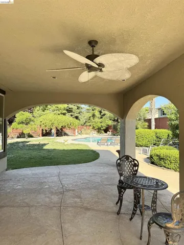 Covered patio featuring an outdoor ceiling fan, recessed lighting, stamped concrete flooring, arched openings, and a lush green lawn leading to a swimming pool