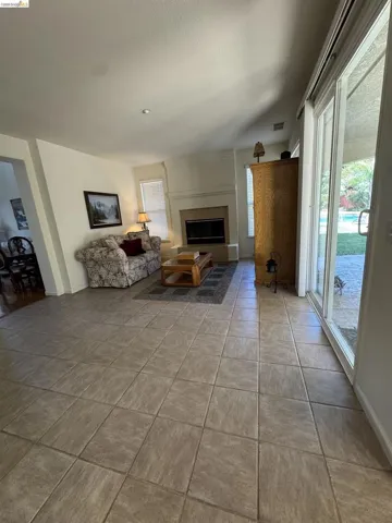 Spacious living area featuring neutral-toned tile flooring, a built-in fireplace with a stone surround and mantel, and recessed lighting
