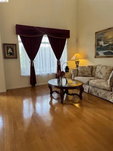 High ceilings accentuate the spaciousness of this room, featuring wood-finish flooring and a large window with custom drapery