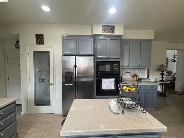 Kitchen featuring gray cabinets, black appliances, a center island, decorative backsplash, and light stone counters