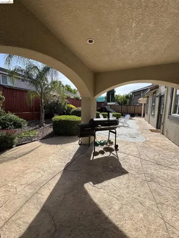 Arched covered patio featuring stamped concrete flooring, a recessed ceiling light, and an expansive garden area with mature landscaping and a privacy fence