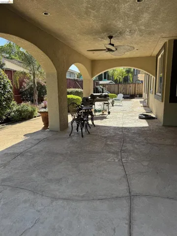 Spacious covered patio featuring stamped concrete flooring, arched structural elements, a ceiling fan, and recessed lighting, extending to an open concrete patio area
