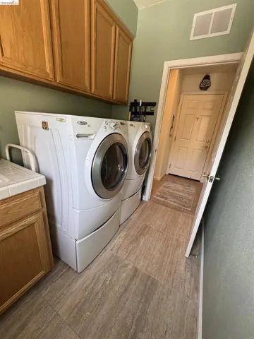 Utility area featuring wood-finish cabinetry, a light-toned countertop, and large format tile flooring