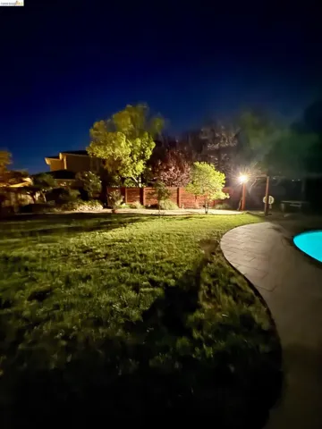 Expansive backyard featuring a manicured lawn, established trees, and a wooden privacy fence