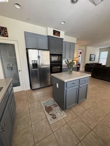 Kitchen featuring a central island with countertop, stainless steel appliances, upper and lower cabinetry, and tiled flooring