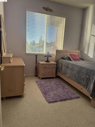 Carpeted room featuring a large window with blinds, soft wall color, and sloped ceiling