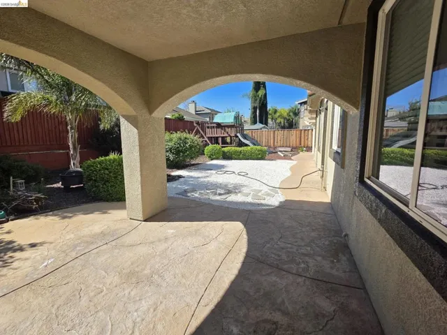 Covered patio featuring stamped concrete flooring, stucco archways, and direct access to the backyard with white gravel accents and lush perimeter landscaping