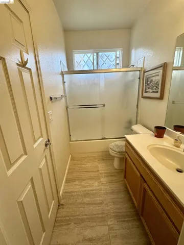Bathroom with vanity, enclosed tub / shower combo, and a textured wall
