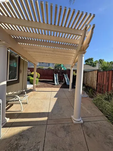 Expansive patio featuring a slatted pergola, decorative columns, and stamped concrete flooring