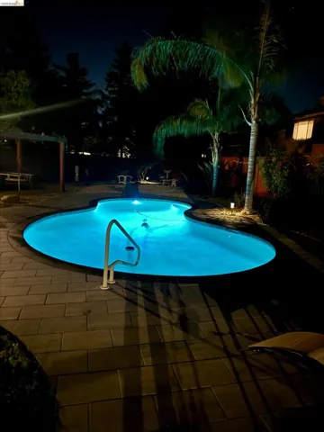 Pool at night with an outdoor pool, a patio area, and a fenced backyard