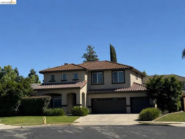 Stucco exterior with a tile roof, featuring a multi-car garage, concrete driveway, and established front landscaping