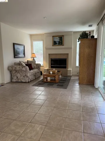 Spacious room featuring neutral tile flooring, a prominent fireplace with a light-toned surround and hearth, and multiple windows with blinds