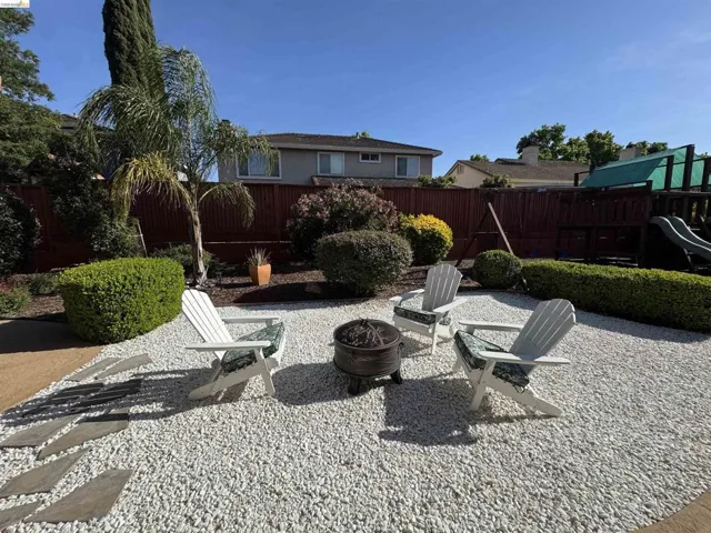 Outdoor gathering space featuring white gravel landscaping, a central fire pit, and mature perimeter hedging
