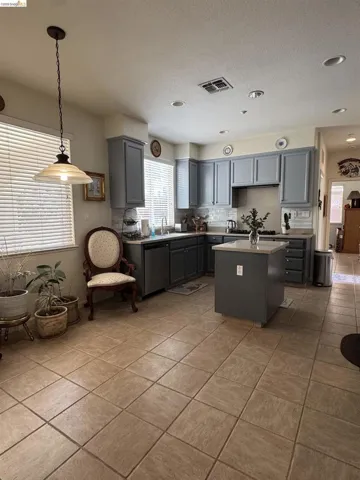 Spacious kitchen featuring gray shaker-style cabinetry, a central island with a light-toned countertop, and stainless steel appliances