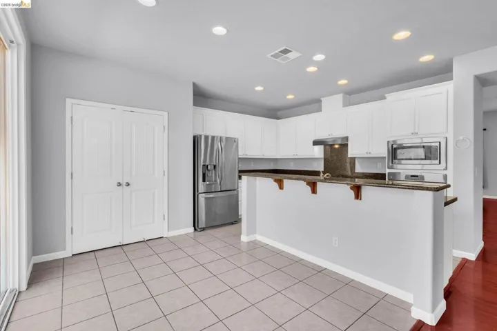 Kitchen featuring stainless steel appliances, a breakfast bar area, white cabinetry, recessed lighting, and dark stone counters