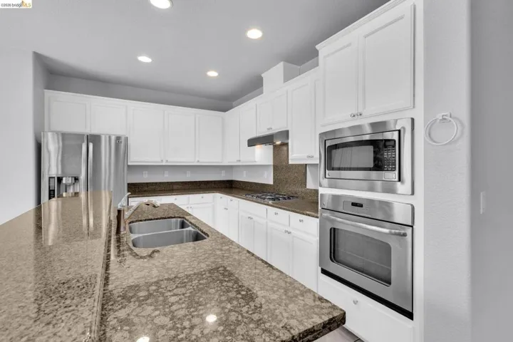 Kitchen with white cabinetry, stainless steel appliances, recessed lighting, a center island with sink, and dark stone counters