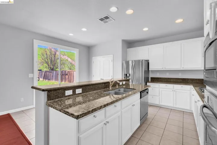 Kitchen with an island with sink, white cabinetry, dark stone counters, recessed lighting, and stainless steel appliances