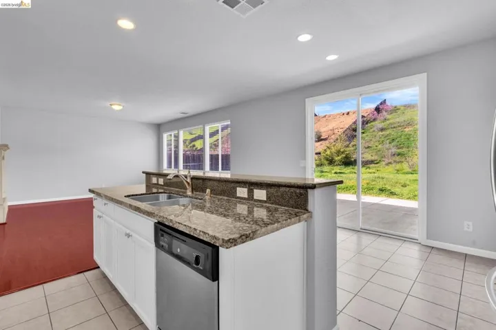 Kitchen with white cabinetry, dishwasher, a kitchen island with sink, dark stone countertops, and recessed lighting