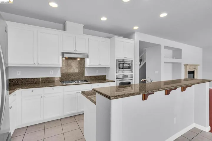 Kitchen with white cabinets, tasteful backsplash, stainless steel appliances, a kitchen breakfast bar, and light tile patterned floors