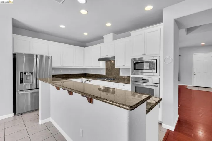 Kitchen featuring white cabinets, a breakfast bar, stainless steel appliances, a center island with sink, and dark stone countertops
