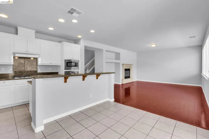 Kitchen featuring light tile patterned floors, white cabinets, a kitchen bar, dark stone countertops, and recessed lighting