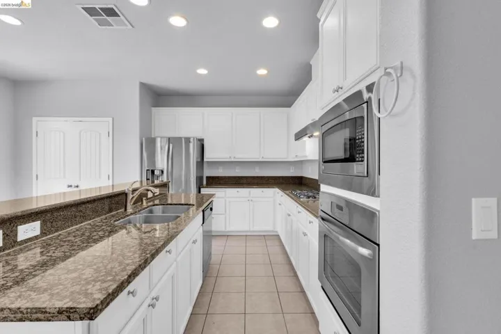 Kitchen with white cabinetry, stainless steel appliances, a kitchen island with sink, recessed lighting, and light tile patterned flooring