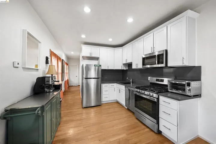 Two tone kitchen featuring dark countertops, stainless steel appliances, light wood finished floors, recessed lighting, and backsplash