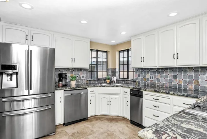 Kitchen with stainless steel appliances, dark stone counters, white cabinets, and recessed lighting