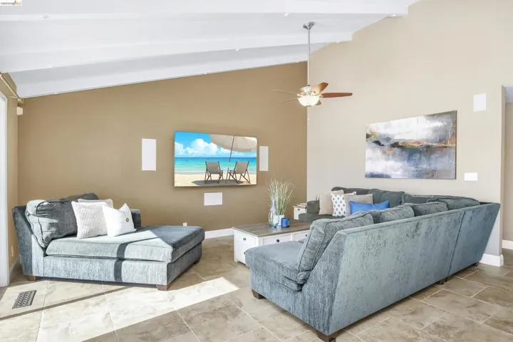 Tiled living room with lofted ceiling with beams and a ceiling fan