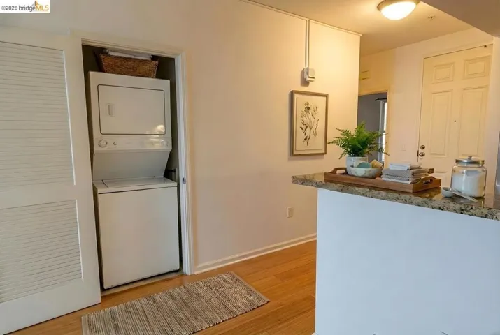 Laundry area with stacked washer / drying machine and light wood-style flooring