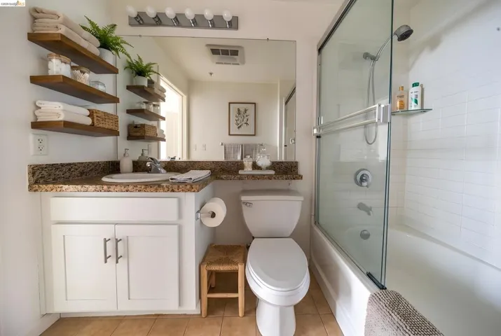Bathroom featuring vanity, bath / shower combo with glass door, and light tile patterned flooring