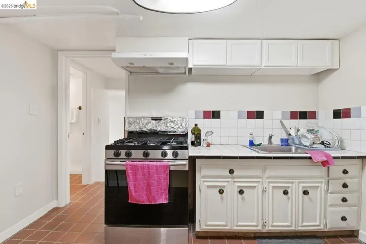 kitchen with tile countertops, gas range, white cabinetry, decorative backsplash, and light tile patterned flooring