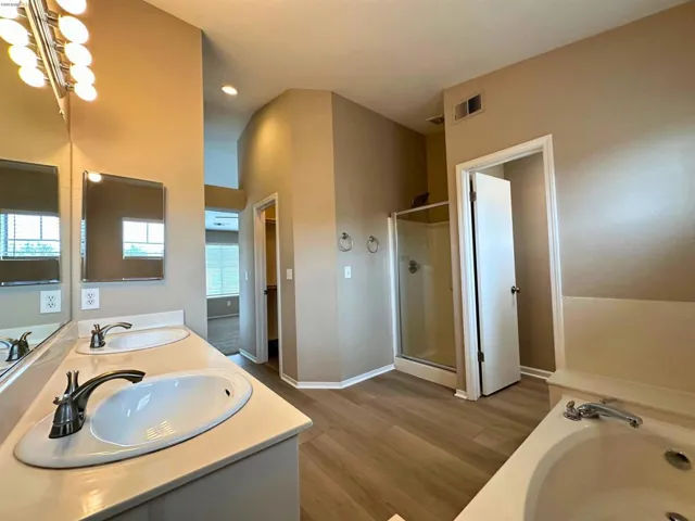 Bathroom with double vanity, dark wood-type flooring, a bath, and a stall shower