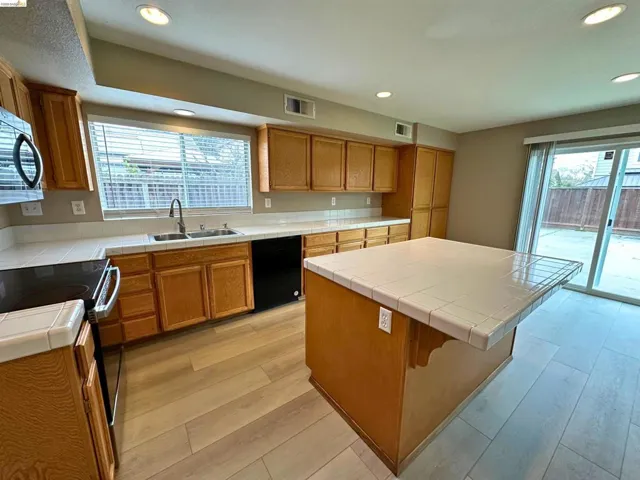 Kitchen with tile countertops, black appliances, wood finish cabinetry, light wood-style flooring, and recessed lighting