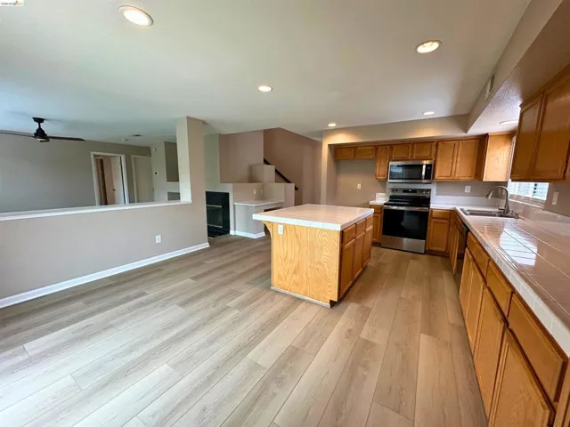 Kitchen featuring tile counters, a center island, stainless steel appliances, wood finish cabinetry, and recessed lighting