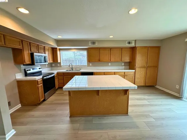 Kitchen featuring tile counters, stainless steel appliances, light wood-style flooring, a kitchen bar, and wood finish cabinetry