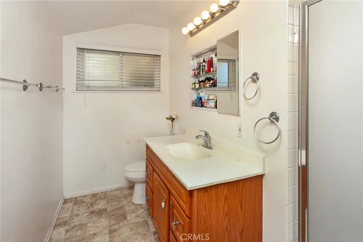 The en suite primary bathroom is thoughtfully designed with a single basin vanity, medicine cabinet, privacy window, Hollywood style lighting, and a glass enclosed tiled step in shower.