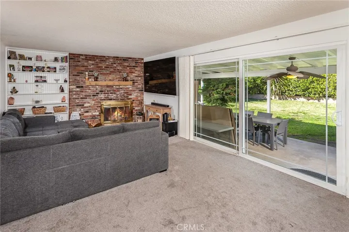 Inside, the family room is warm and welcoming with a dramatic floor to ceiling brick fireplace, built in bookshelves, carpeting, and a sliding glass door that opens to the backyard, creating a seamless connection to outdoor living.