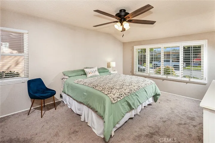 The primary bedroom includes plantation shutters, multiple windows, carpeting, and a lighted ceiling fan.