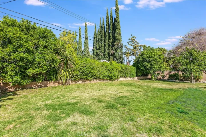 The backyard is a standout feature, offering a spacious and private setting with a lush green lawn, mature trees including citrus, abundant shrubbery, and colorful raised flowerbeds. A covered patio with a lighted ceiling fan creates an ideal space for relaxing or entertaining.