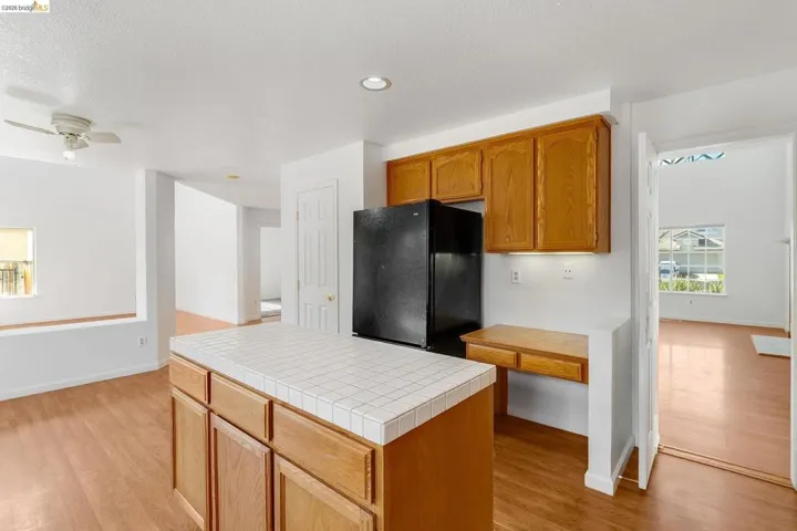 Kitchen with freestanding refrigerator, tile countertops, light wood-type flooring, ceiling fan, and wood finish cabinetry