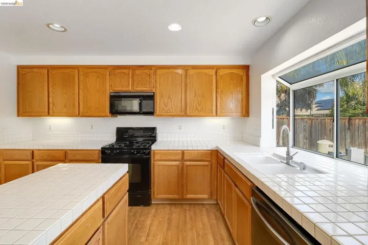 Kitchen with black appliances, wood finish cabinets, recessed lighting, light wood-type flooring, and tile counters