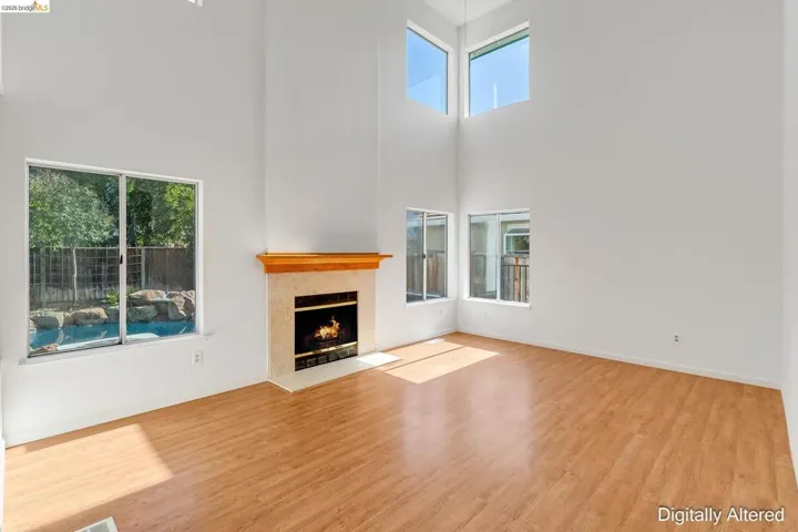 Unfurnished living room featuring light wood-style floors, a fireplace with flush hearth, healthy amount of natural light, and a high ceiling
