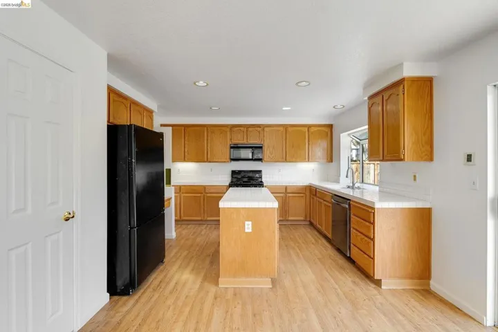 Kitchen with tile countertops, black appliances, wood finish cabinets, a center island, and light wood-style floors