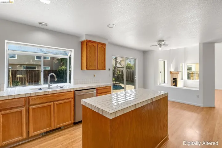 Kitchen featuring light wood-style floors, wood finish cabinetry, a warm lit fireplace, stainless steel dishwasher, and a textured ceiling