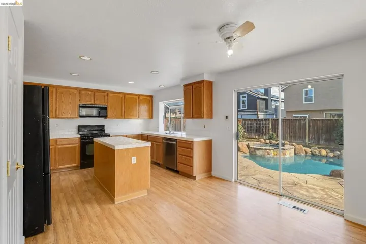 Kitchen featuring tile countertops, a ceiling fan, black appliances, a kitchen island, and plenty of natural light