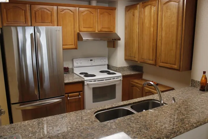 Kitchen featuring freestanding refrigerator, white range with electric cooktop, dark stone counters, and wood finish cabinetry